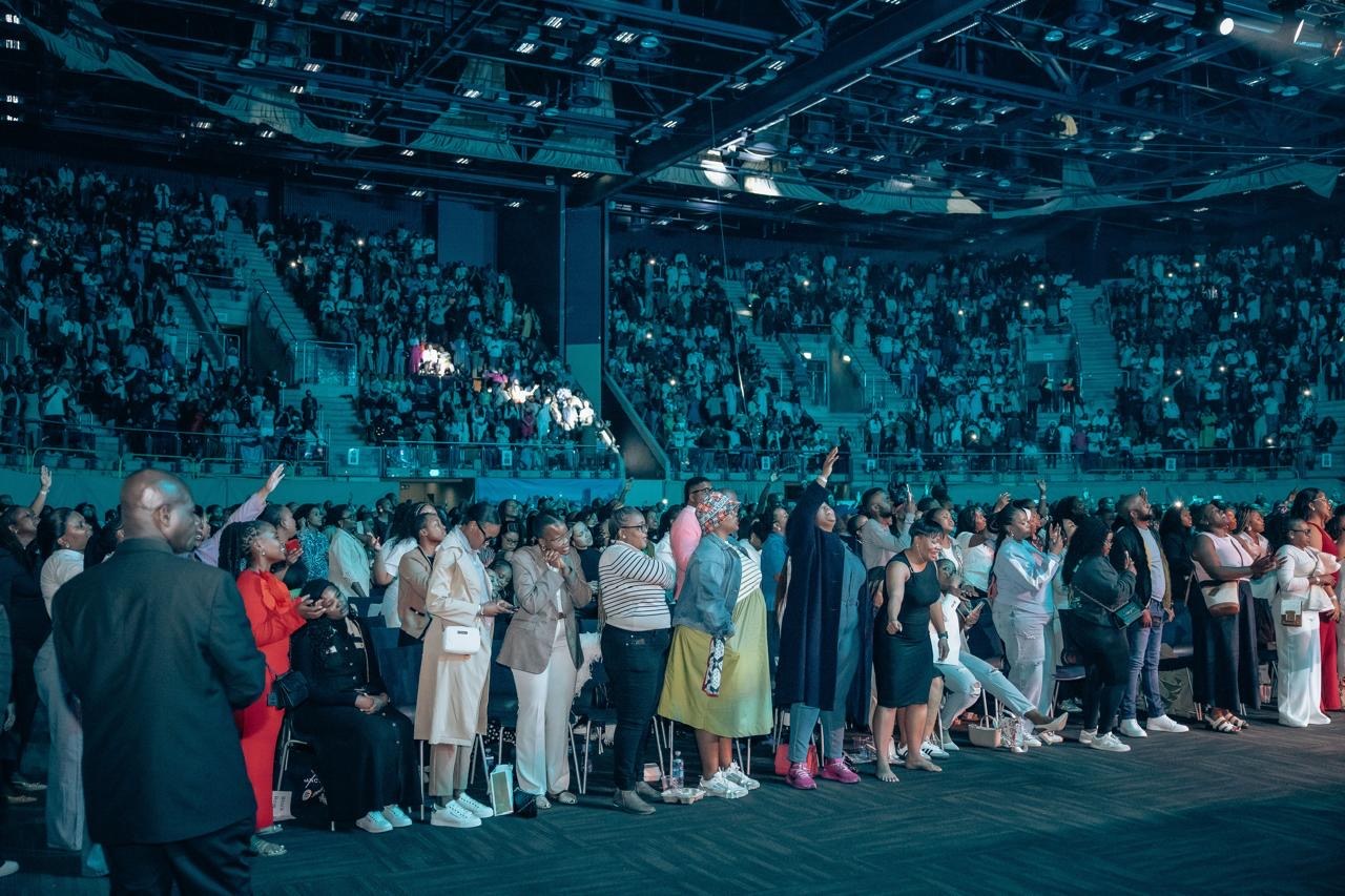 A wide arena photograph of Xolly with a gathered congregation