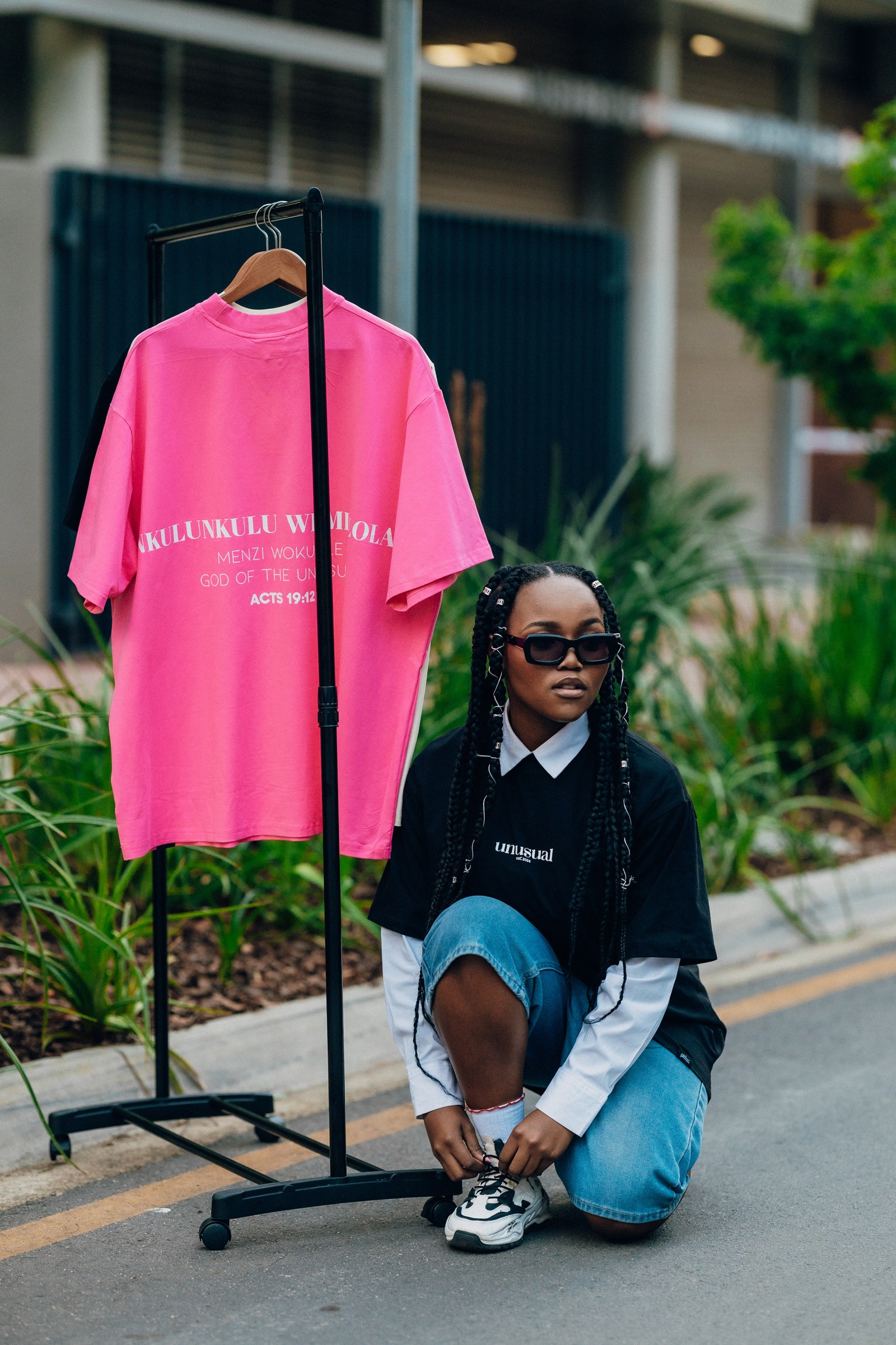 A pink statement T-shirt on an apparel rack with a model